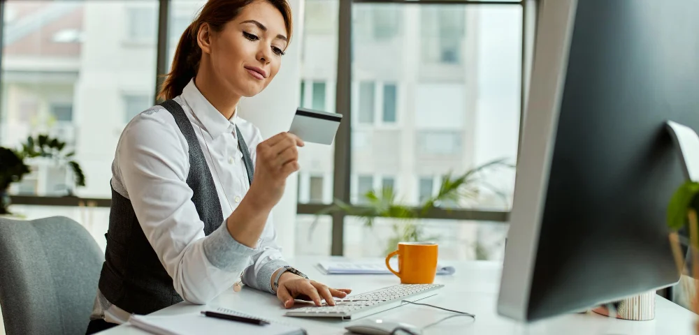 escriturário de banco aprovado no concurso BNB segurando um cartão e trabalhando em frente ao computador